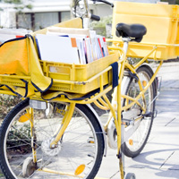 Abgebildet ist das vollbeladene, gelbe Fahrrad eines Briefträgers.